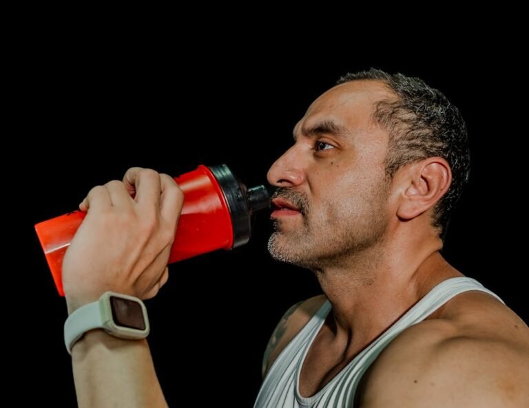 Fit adult male drinking from shaker bottle, fitness focus, black background.